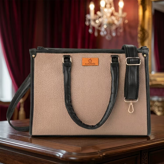 Beige handbag with black handles and strap on a wooden surface with a chandelier in the background