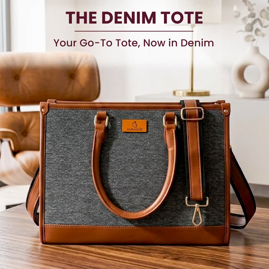 Denim tote bag with brown handles and trim on a wooden surface, with a blurred indoor background.